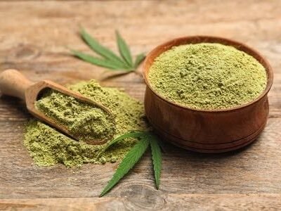 Organic green hemp powder in a wooden bowl with hemp leaves on rustic wood background.
